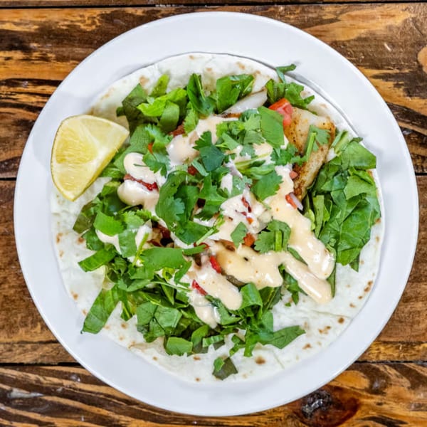 Overhead view of a fish taco with lettuce, cilantro, and sauce, served with a lime wedge.