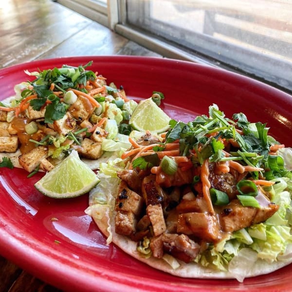 Two DGT Tacos, one with tofu and one with chicken, on a red plate with lime wedges.