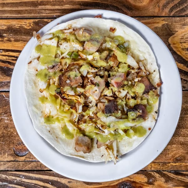 Overhead view of a taco with meat, shredded cabbage, and green sauce on a white plate.