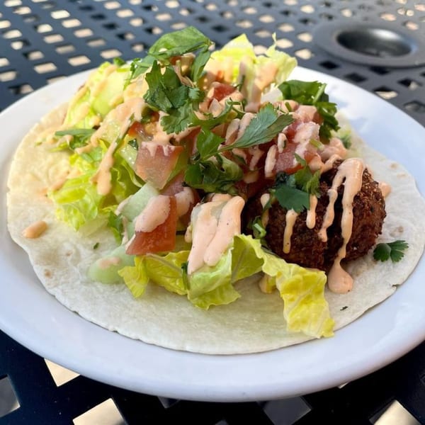 A DGT Tacos falafel taco with lettuce, tomatoes, cilantro, and a creamy sauce on a white plate.