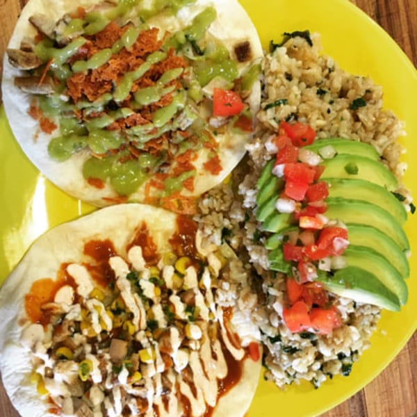 Two DGT Tacos with rice, avocado, and pico de gallo on a bright yellow plate.