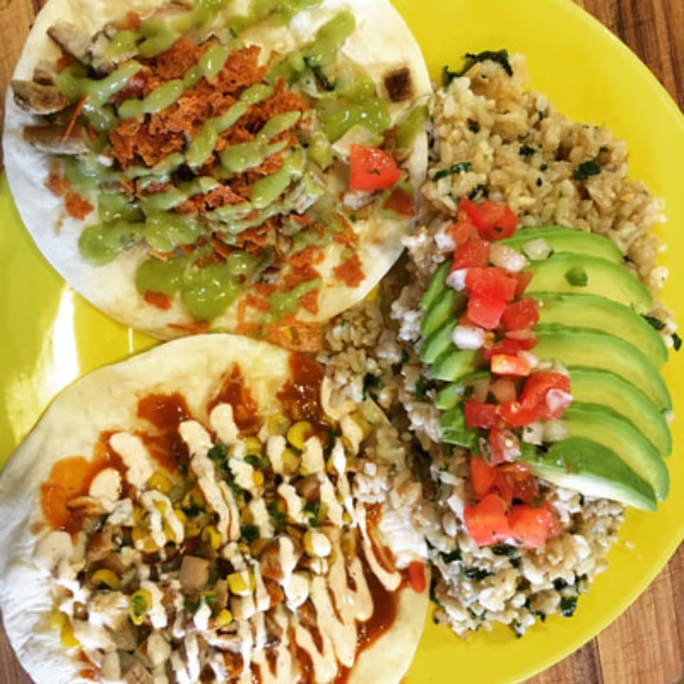 Two DGT Tacos with rice, avocado, and pico de gallo on a bright yellow plate.