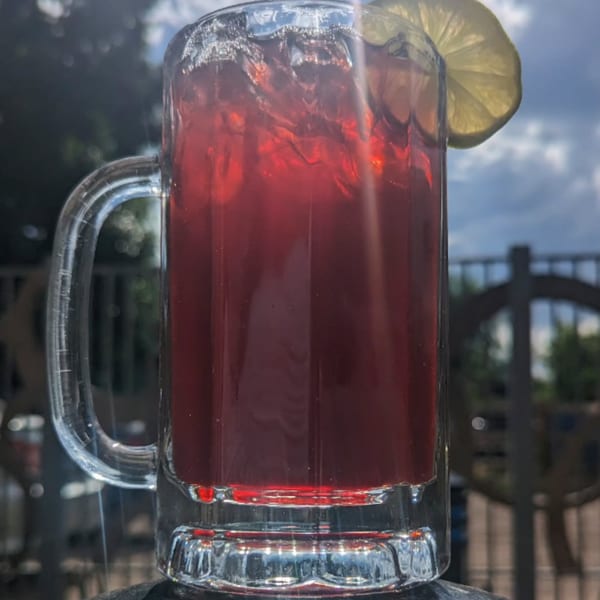 A large glass mug of DGT Tacos' red agua fresca with ice and a lemon slice, outdoors.