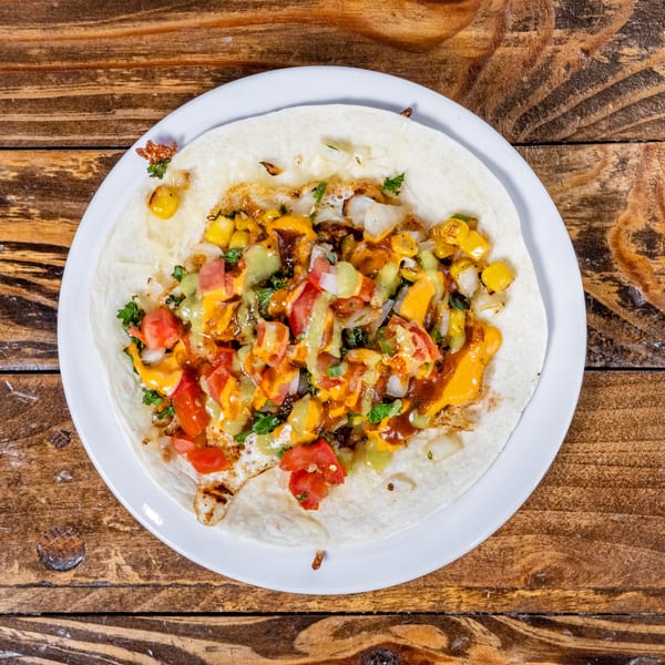A DGT Tacos tortilla with corn, tomatoes, onions, and sauces on a white plate.