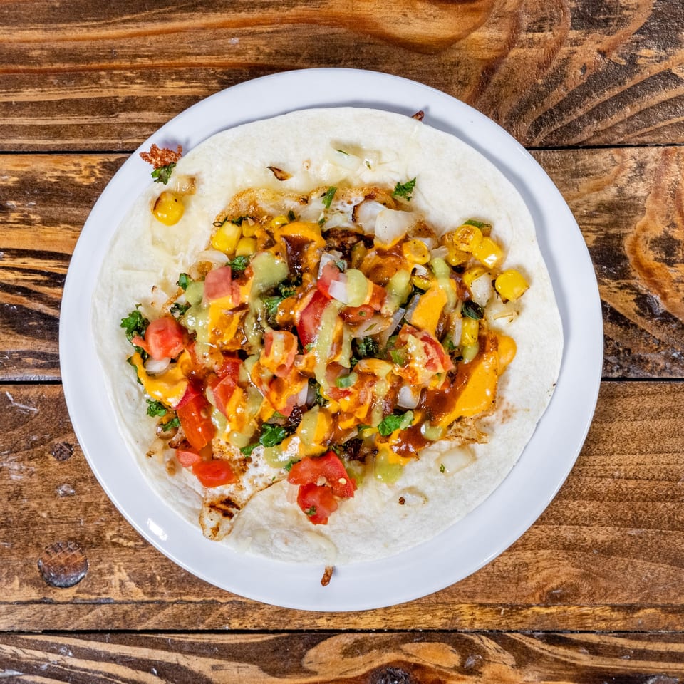 A DGT Tacos tortilla with corn, tomatoes, onions, and sauces on a white plate.