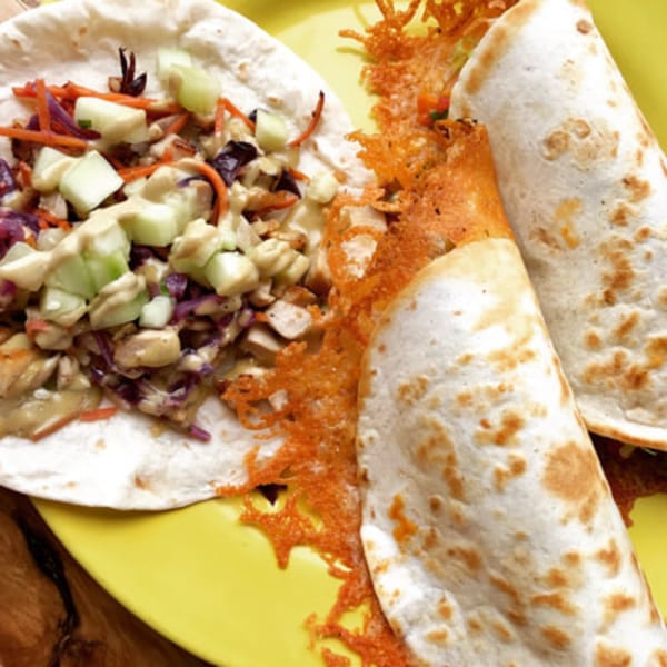 Two DGT Tacos on a yellow plate, one open with toppings, the other rolled with crispy cheese.
