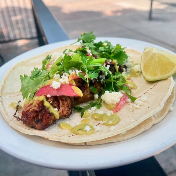 A DGT Tacos Fort Collins taco with meat, cilantro, cheese, and sauce, served with a lime wedge.