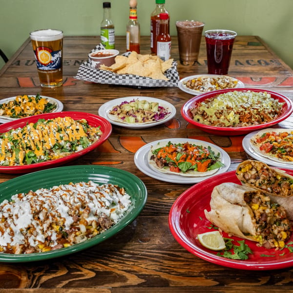 A wooden table laden with various DGT Tacos dishes, including tacos, burritos, and bowls, with drinks.